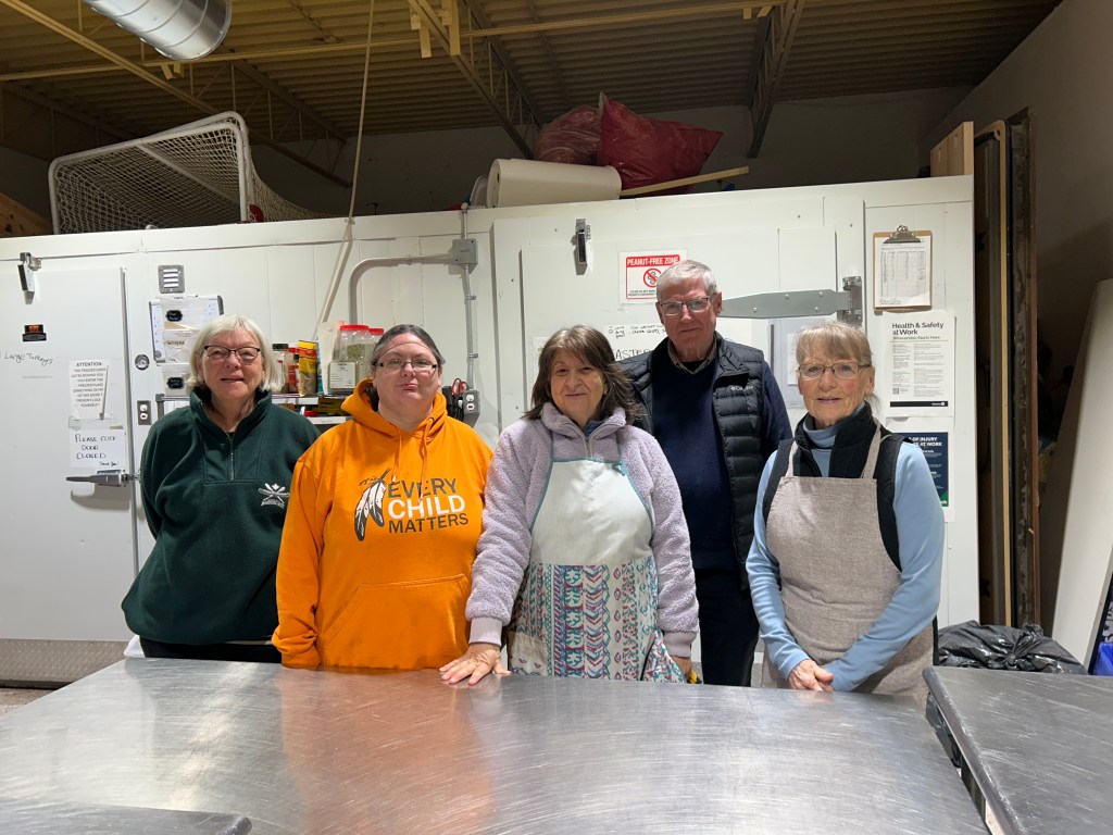 Five smiling people standing in a commercial kitchen.  