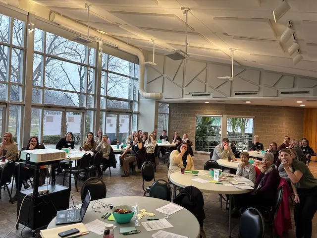 A group of people seated at round tables in a bright event space bite into apples during the Big Crunch celebration, showing collective support for healthy school food alongside educators, growers, and community partners.