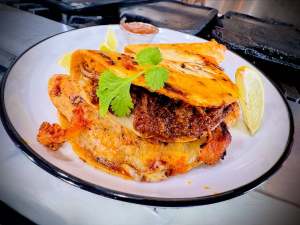Grilled corn tortilla filled with slow-cooked meat and melted cheese, topped with fresh cilantro and served with lime on a plate at IvanoPoblano.