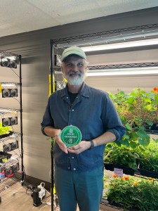 Joe Gansevles, Coordinator of Urban Agriculture and Environmental Sustainability, holding a Food Champion award inside an indoor growing space.