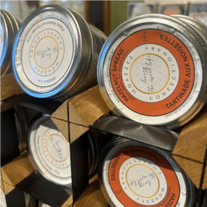 Metal tins of hazelnut spread stacked in a wooden display rack, with orange-and-white labels visible on the front containers.