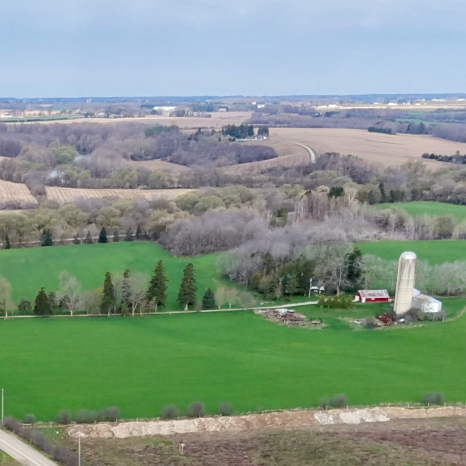Aerial view of a family farm in Middlesex County, Ontario, with bright green fields, a red barn, and grain silo surrounded by trees