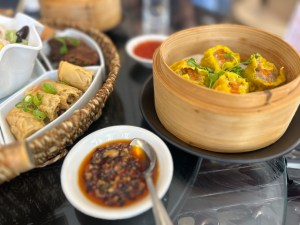 A close-up of steamed dumplings and other dishes served with a savoury dipping sauce, arranged on a table at Jing Jing Market & Eatery.